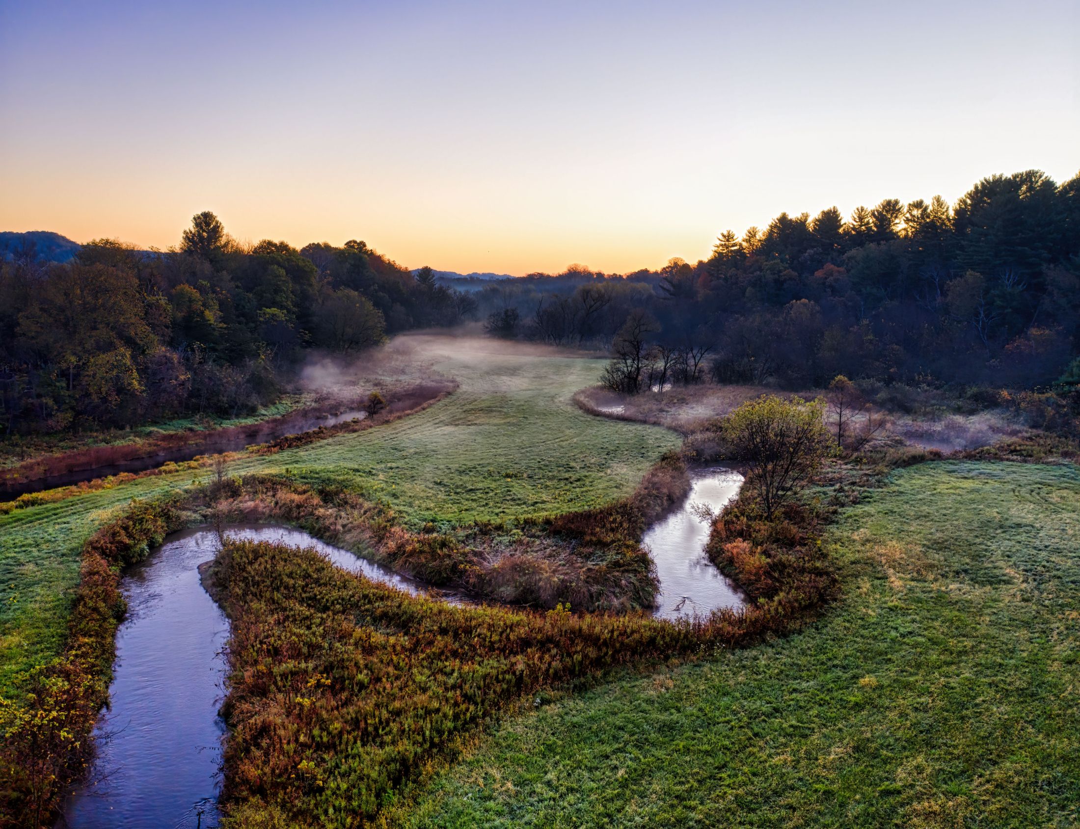 Aerial view of a creek winding through meadow and forest